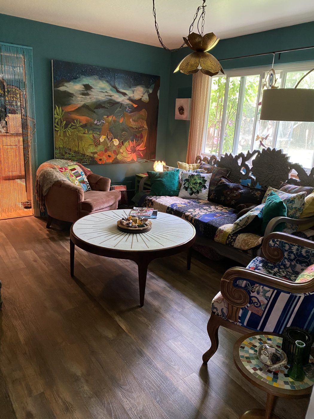 A living room with a mountain painting, patterned sofa and round coffee table.